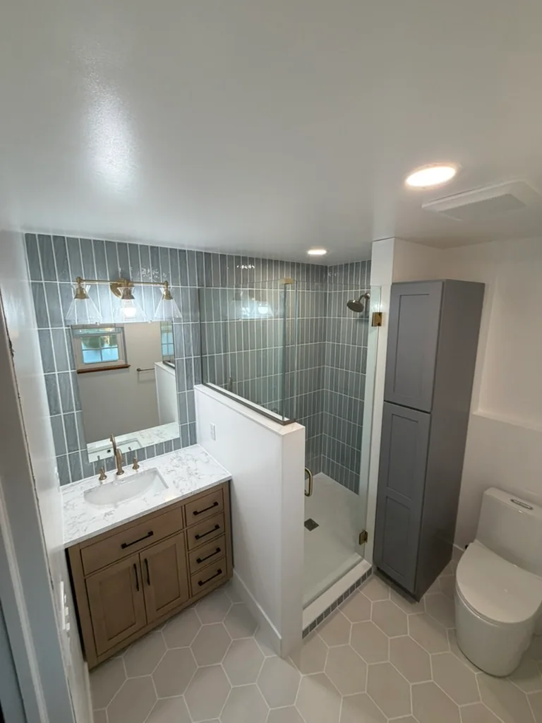 Remodeled bathroom in Sylvania, Ohio with a blue tile shower, glass enclosure, wood-tone vanity, and hexagon floor tile.